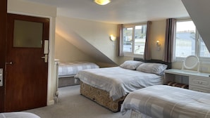 A bedroom with two beds, a window with curtains, a bedside table with a mirror, and a door. - Lamplighter Guesthouse (Plymouth)