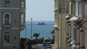 A coastal street with buildings, parked cars, and a ship in the distance. - Lamplighter Guesthouse (Plymouth)