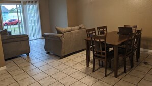 Uma sala de jantar com uma mesa e cadeiras, um ventilador de teto e uma porta de vidro deslizante que dá para um pátio.