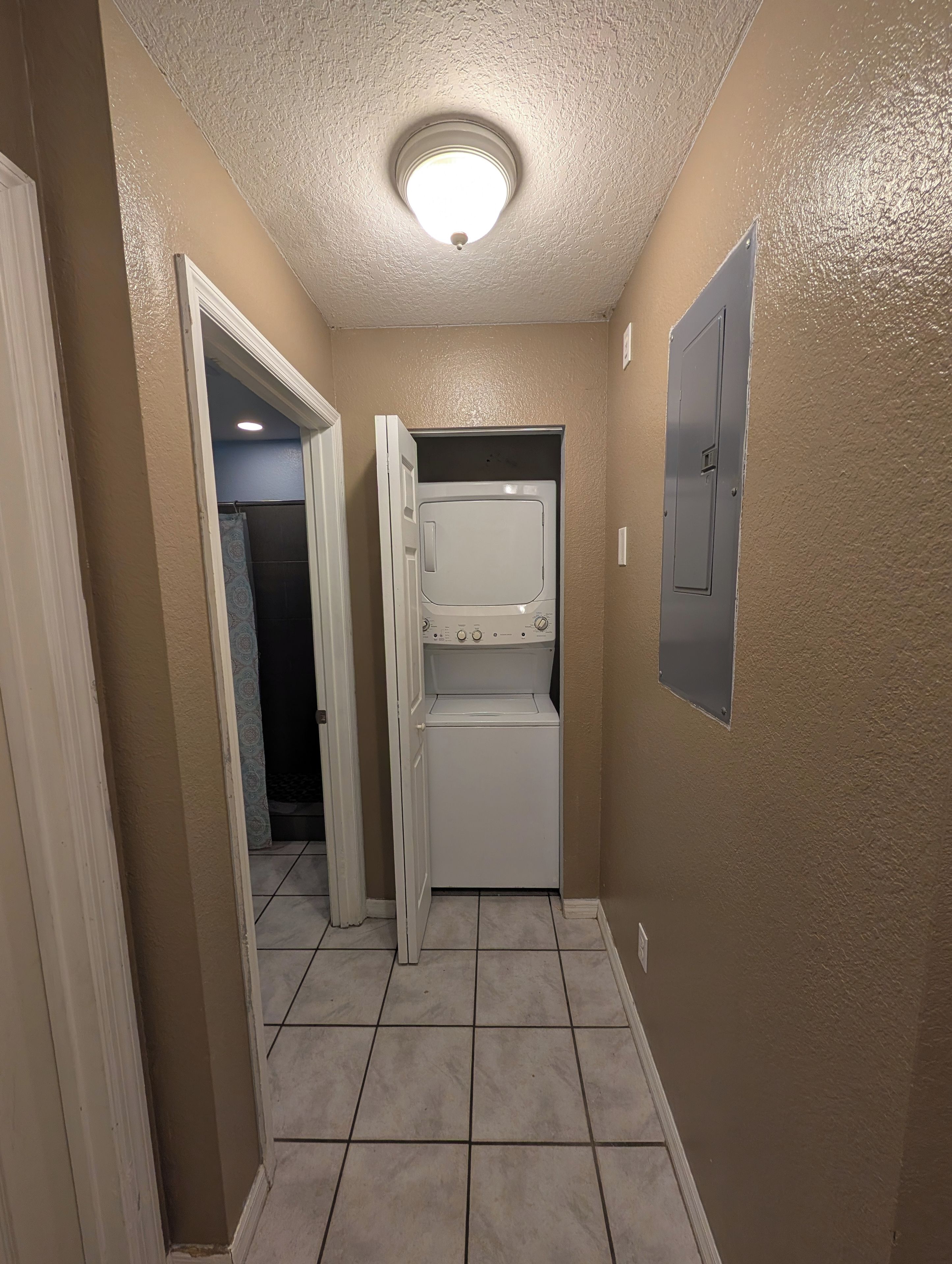 Un cuarto de lavado con lavadora y secadora, una puerta que da a otra habitación y una lámpara en el techo.