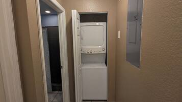Un cuarto de lavado con lavadora y secadora, una puerta que da a otra habitación y una lámpara en el techo.