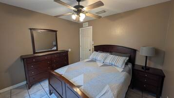 Un dormitorio con cama, cómoda, espejo, ventilador de techo y lámpara de noche.