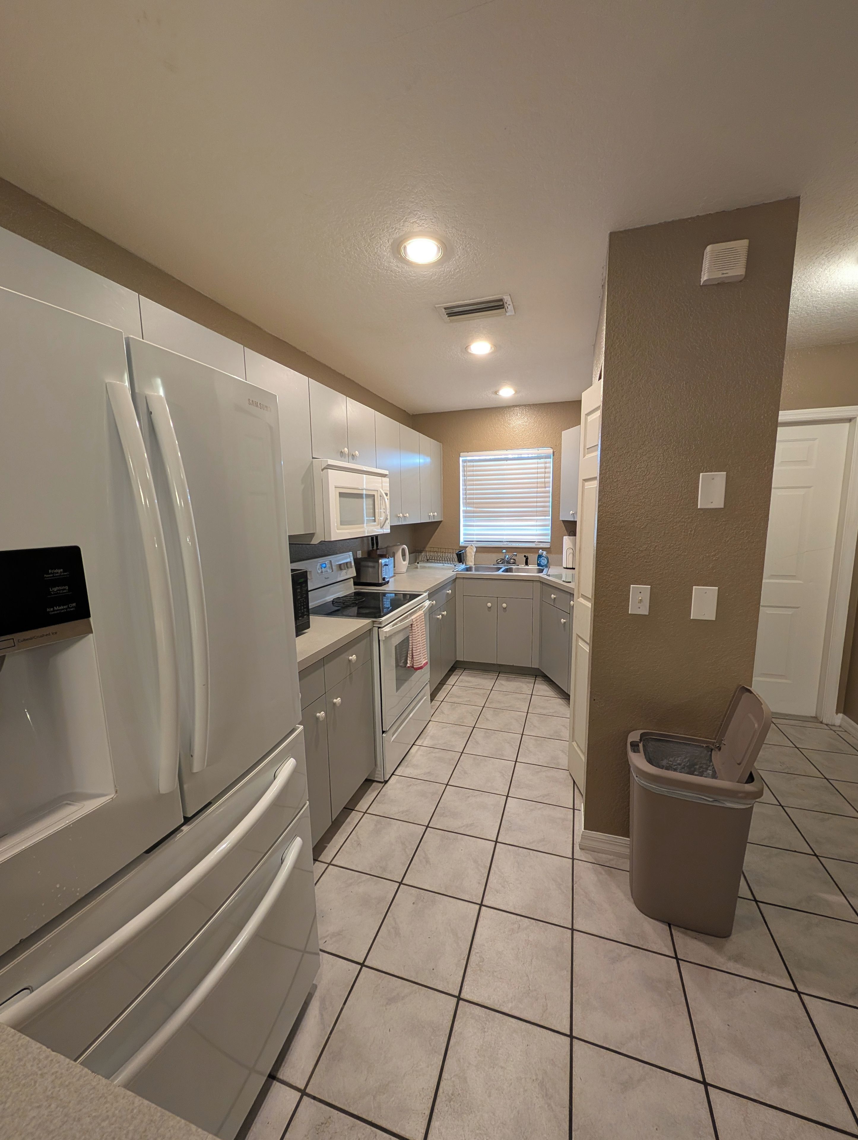 Una cocina equipada con refrigerador, microondas, horno y un bote de basura.