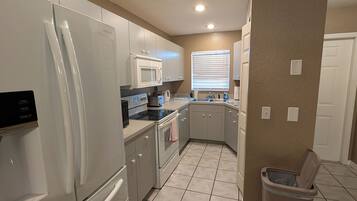 Una cocina equipada con refrigerador, microondas, horno y un bote de basura.