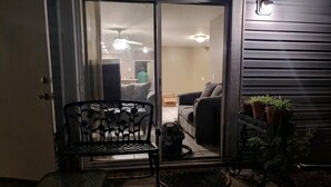 Uma área de pátio com um banco e mesa de metal, uma porta de correr e vasos com plantas.