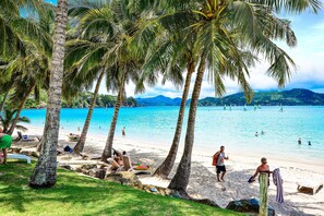 A beach with palm trees, clear blue water, and people sunbathing.