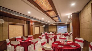 Une salle de conférence avec des tables rondes, des chaises blanches ornées de rubans rouges et un écran de projection.