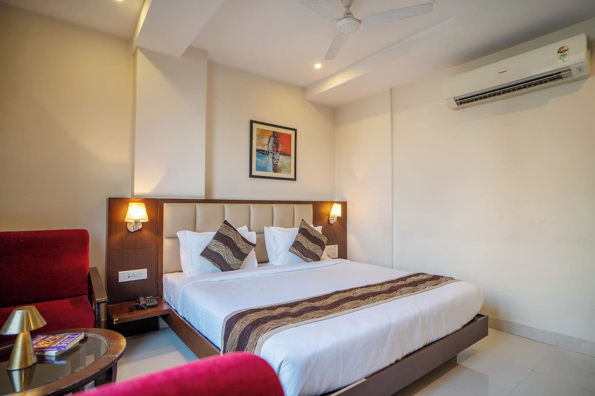 A hotel room with a bed, a red armchair, a bedside table with a lamp, and a ceiling fan.