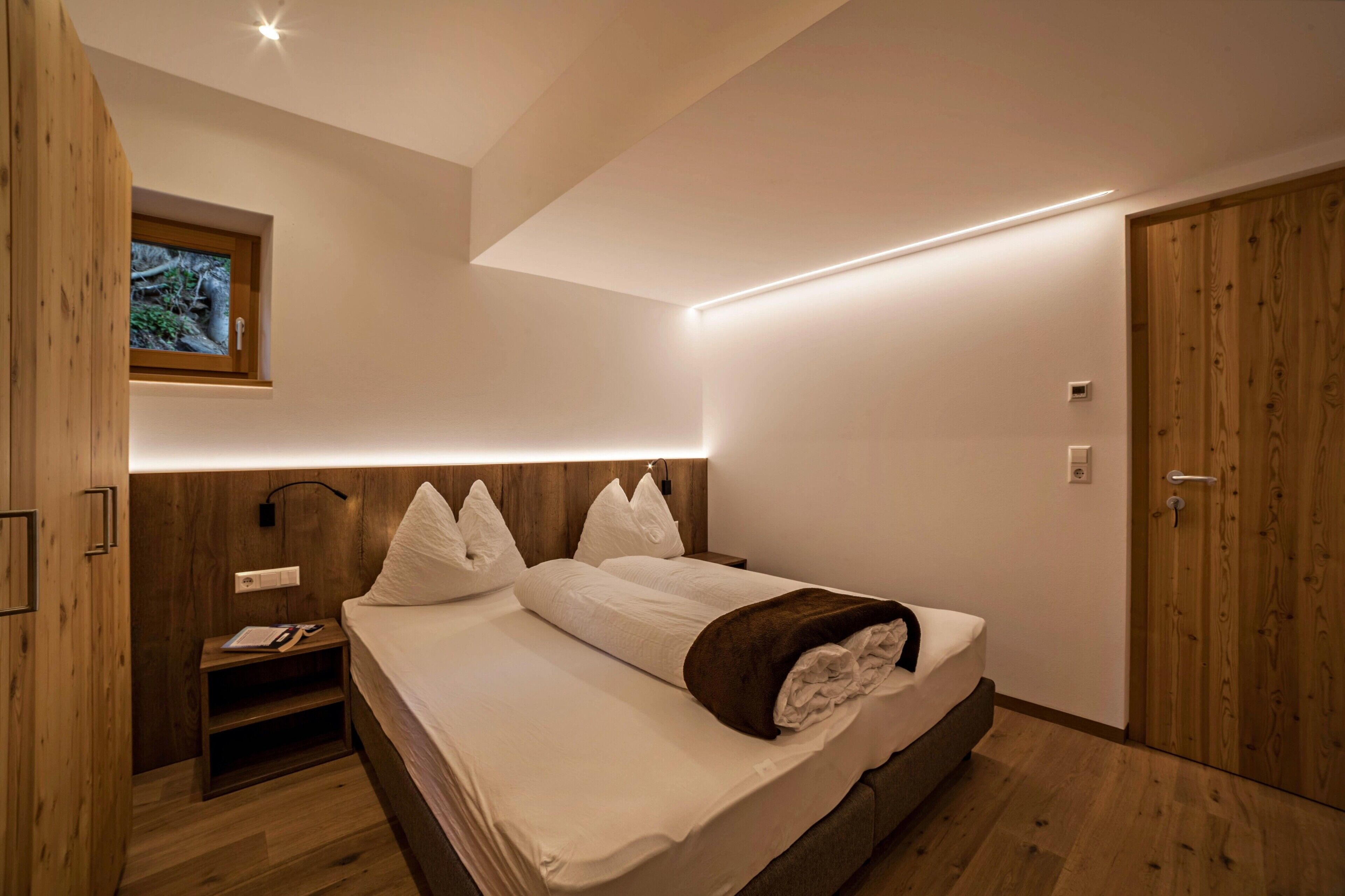 Een moderne slaapkamer met een houten hoofdbord, een nachtkastje met een lamp en een nachttafeltje.