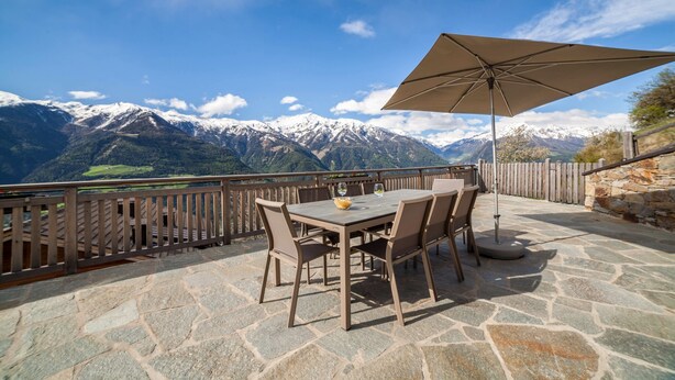 Eine Terrasse im Freien mit Steinboden, einem Tisch und Stühlen sowie einem großen Sonnenschirm.