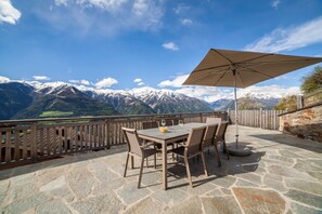 En udendørs terrasse med flisebelægning, et bord med stole og en stor parasol.