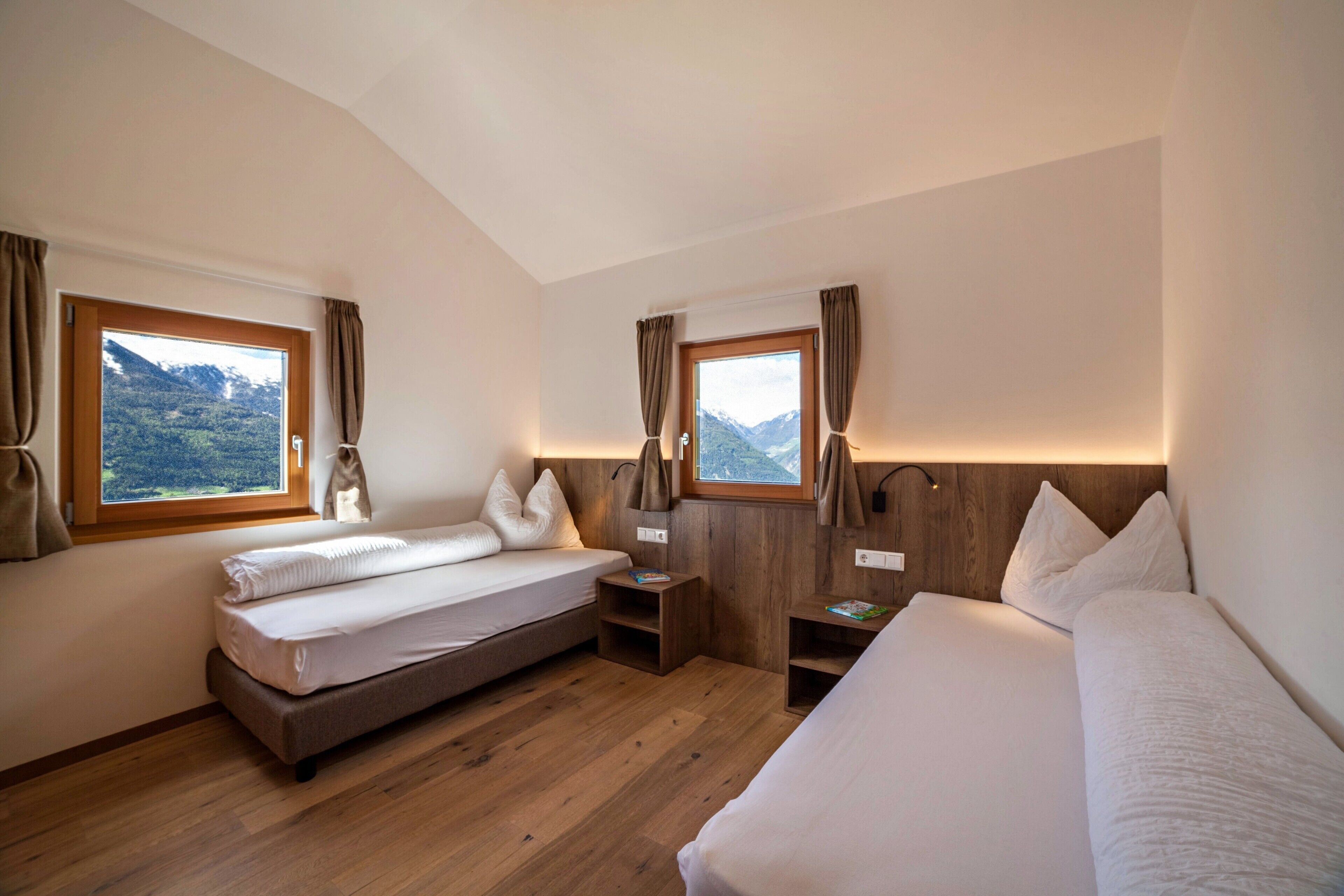Une chambre avec deux lits, un plancher en bois et une vue sur les montagnes par les fenêtres.