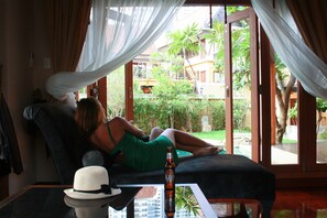 Enjoy a serene view of the lush garden from the comfort of this room, featuring a sofa and a table with a refreshing drink.