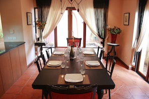 Enjoy meals in this dining area with a long table set for a meal, surrounded by natural light and greenery.