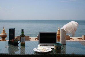 A glass table with a laptop, a plate with food, a bottle, and a mug, overlooking a body of water.