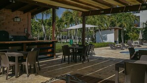 Ein Außenbereich mit Terrasse, Grill, Tischen und Stühlen. Im Hintergrund ist ein Pool zu sehen.
