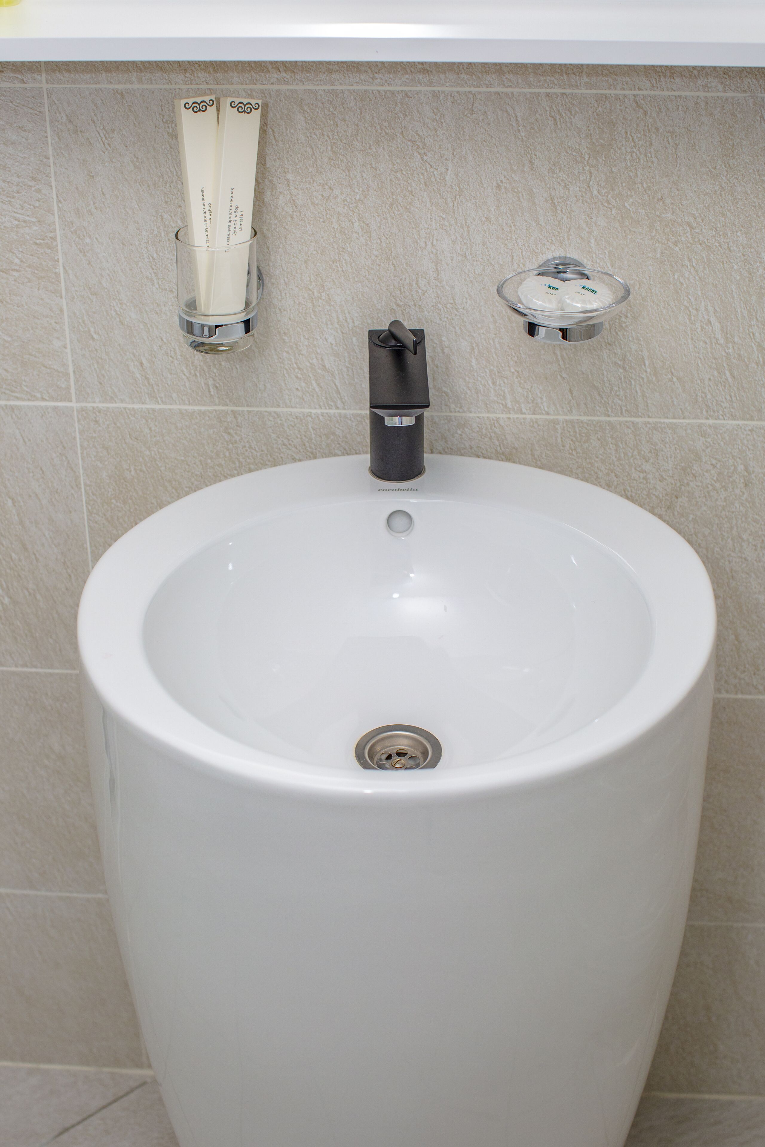 A large, white pedestal sink with a black faucet and a drain.