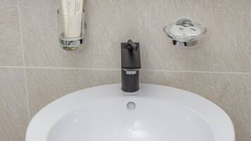 A large, white pedestal sink with a black faucet and a drain.
