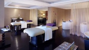 Een moderne spa ruimte met twee massagetafels, een badkuip en een wastafelmeubel.
