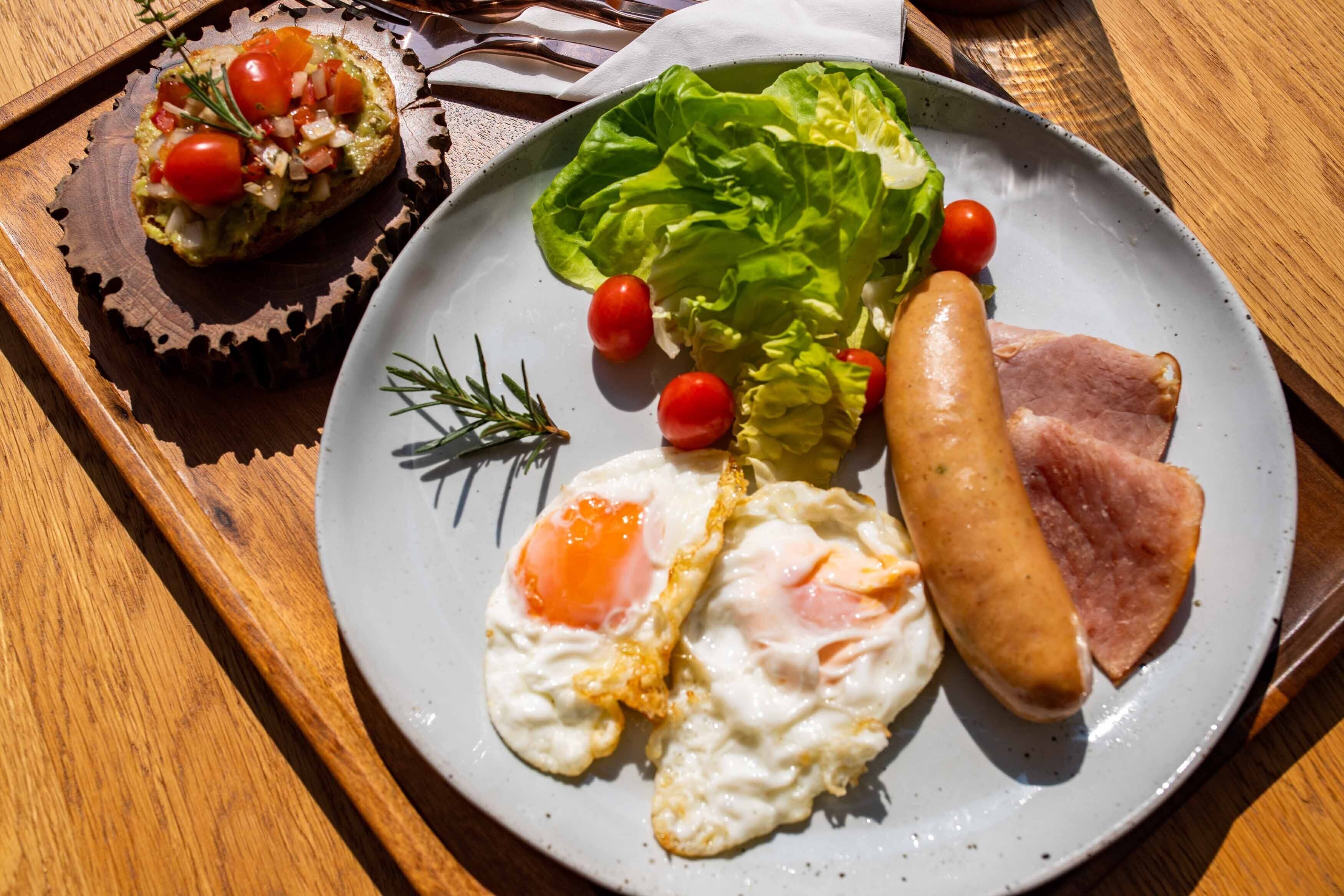 Un plato con huevos, salchicha, jamón, lechuga y tomates cherry.