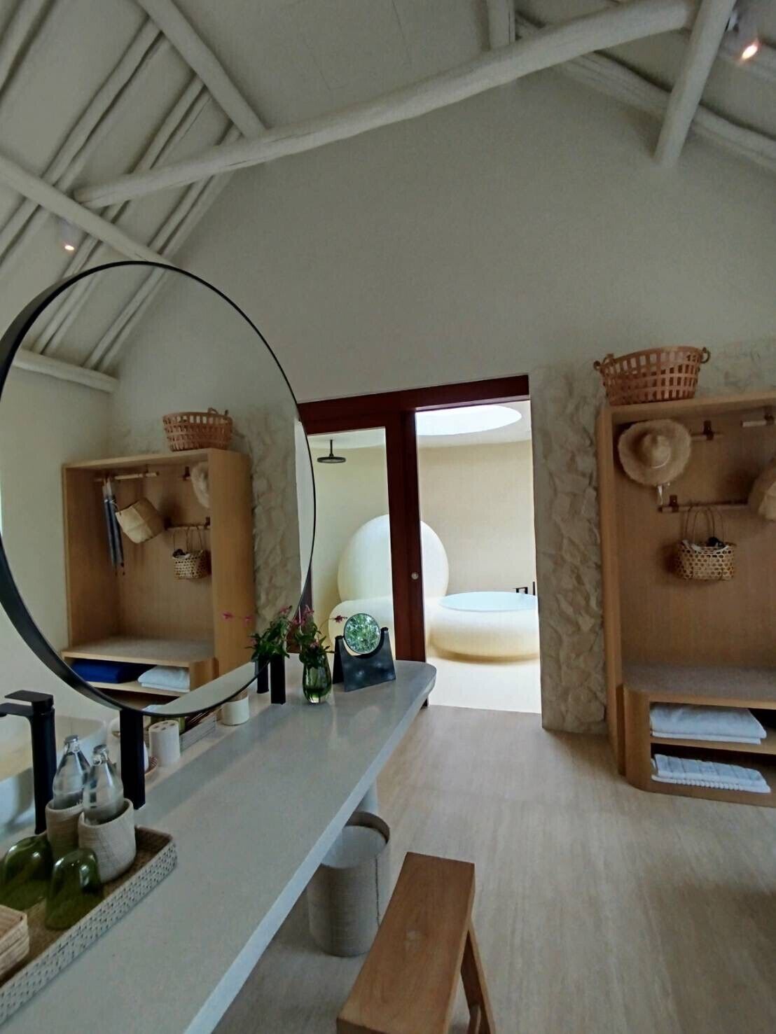 A bathroom with a large mirror, wooden shelves, a bench, and a towel rack.