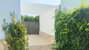Un espace extérieur abrité, doté d’un sol carrelé, d’un portail gris et d’un feuillage verdoyant et luxuriant.