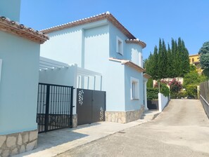 A light blue building with a tiled roof, a gated entrance, and a stone base. - 0687 Villa Benicadims Jazmin (Beniarbeig)