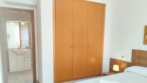 Une chambre à coucher comprenant un lit, une table de chevet, une lampe, une armoire en bois et une salle de bain avec un lavabo et un miroir.