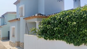 Une rangée de bâtiments bleu clair aux murs blancs et aux toits en tuiles, un mur blanc recouvert de lierre vert et un ciel dégagé.