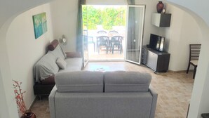 Un salon chaleureux avec un canapé, un téléviseur et un coin repas visible à travers une porte vitrée.