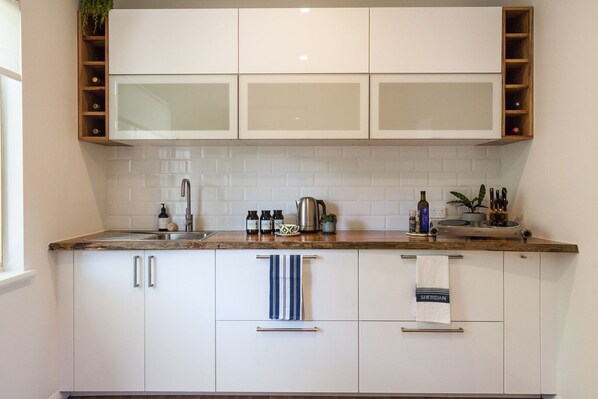 A modern kitchen with white cabinets, a stainless steel sink, and a wooden countertop.