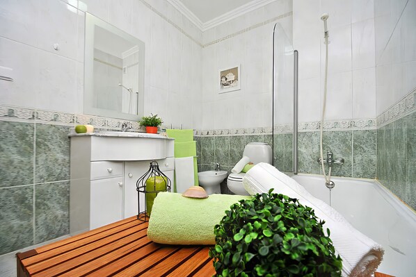 Une salle de bain avec un banc en bois, une serviette verte, une plante en pot, un bidet et une baignoire.