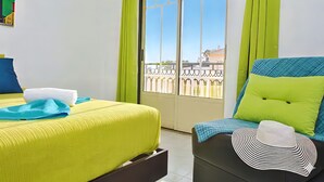 Hotelkamer met een bed, een stoel, een balkon met hekwerk en een raam.