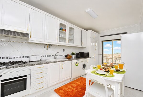 Une cuisine moderne avec des meubles blancs, une cuisinière à gaz, un four à micro-ondes et un coin repas avec une table mise pour le petit-déjeuner.