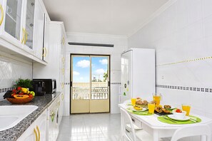 Une cuisine avec des meubles blancs, une table à manger avec des sets de table verts, et une vue à travers la porte.
