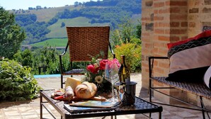 A table set outdoors with a view of rolling hills, a wicker chair, and a cushioned bench.