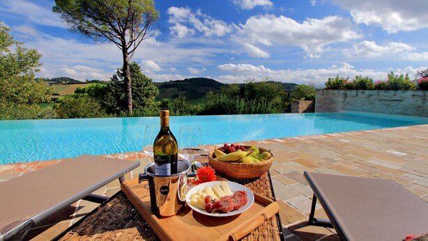 A poolside setting with a bottle of wine, a bowl of fruit, and a plate of cheese and grapes.