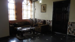 A living room with a sofa, a coffee table, and a patterned rug. There is a door and a wall with a framed picture. - Calabar Grand Hotel (Calabar)