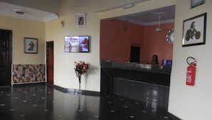 A lobby with a reception desk, a television, a fire extinguisher, and a vase of flowers. - Calabar Grand Hotel (Calabar)