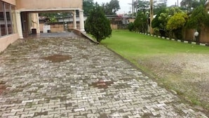 A courtyard with a paved walkway leading to a building entrance, surrounded by greenery and palm trees. - Calabar Grand Hotel (Calabar)