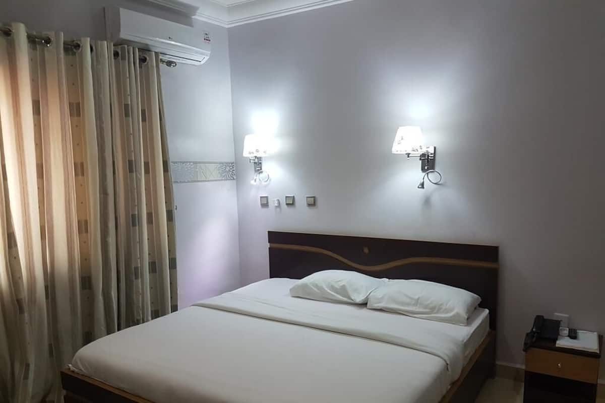 A hotel room with a bed, curtains, wall-mounted lights, and a nightstand.