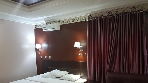 A hotel room with a bed, bedside lamps, an air conditioner, and a dark-colored sofa. - Calabar Grand Hotel (Calabar)