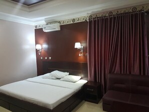 Una camera d'albergo con un letto, due abat-jour, un condizionatore d'aria e un divano scuro.