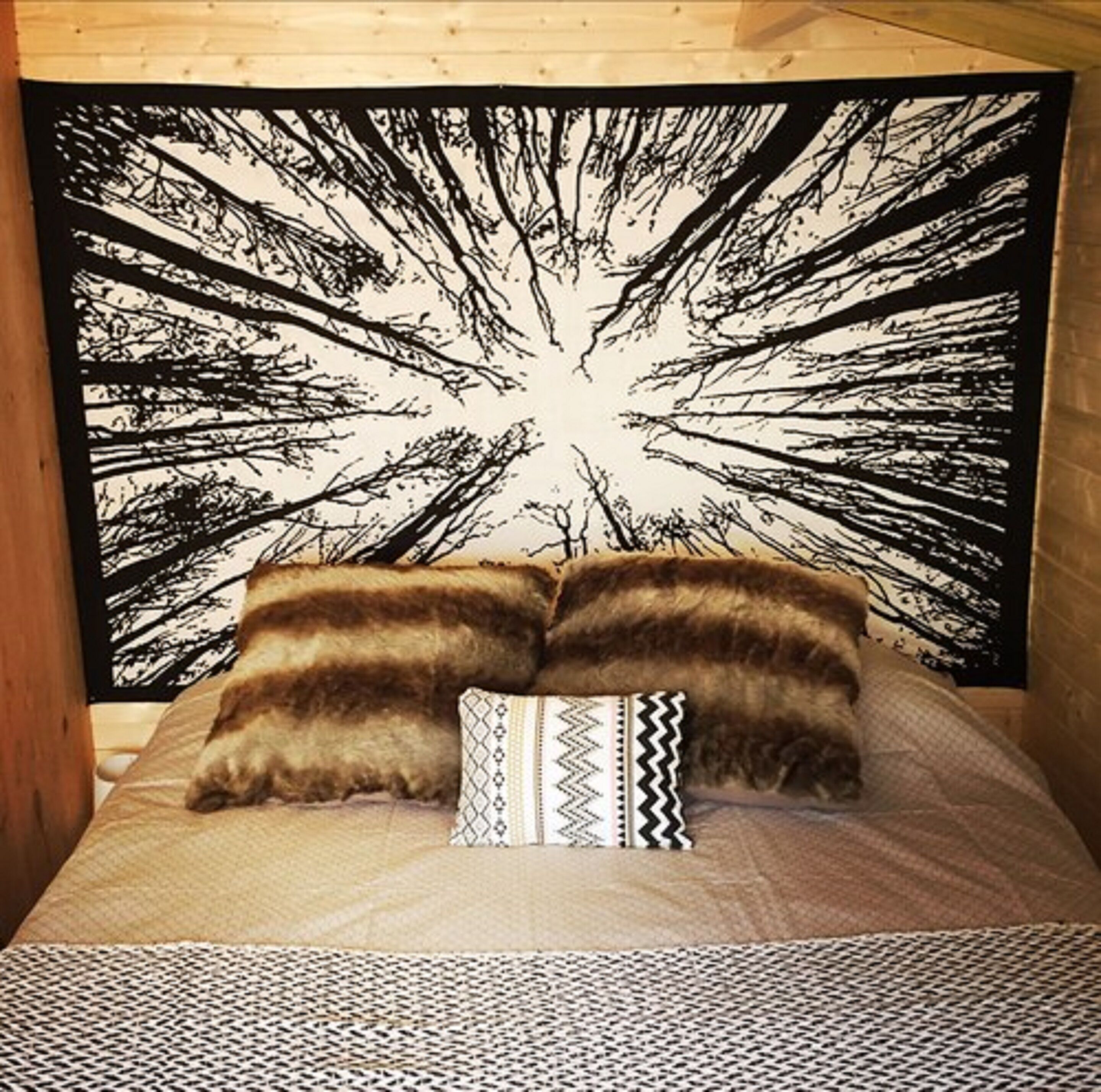 A bed with a black and white abstract tapestry, two brown pillows, and a patterned pillow.