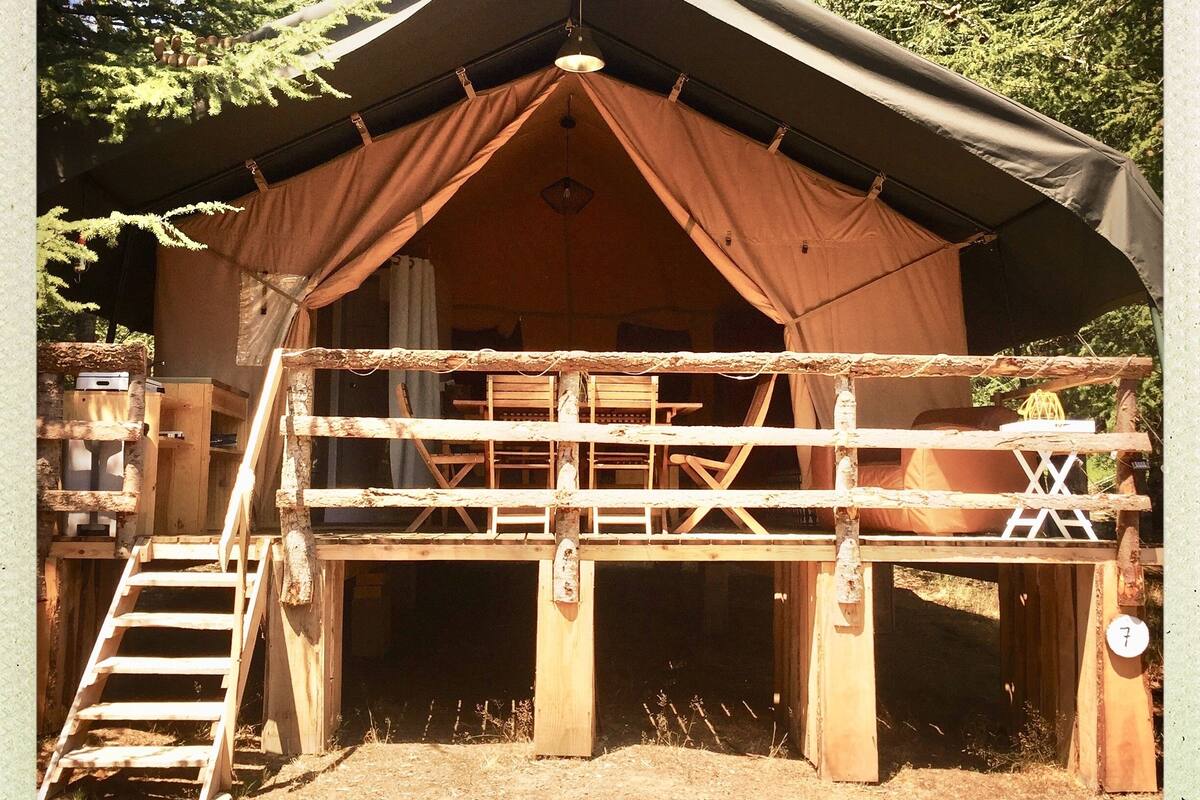 Una cabaña de madera rústica con un balcón, una escalera que lleva a la entrada y una pequeña mesa en la terraza.