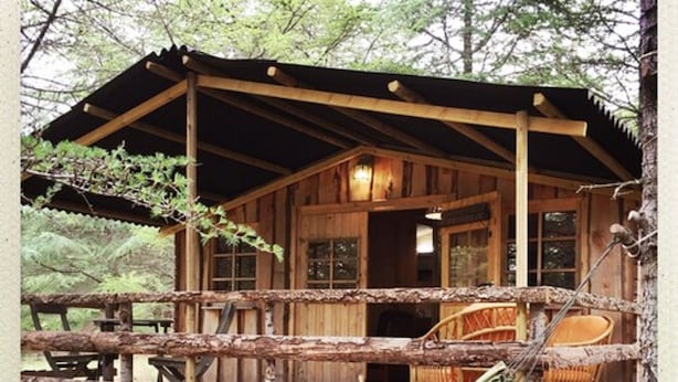 Une cabane en bois avec une véranda, un hamac et un coin repas.