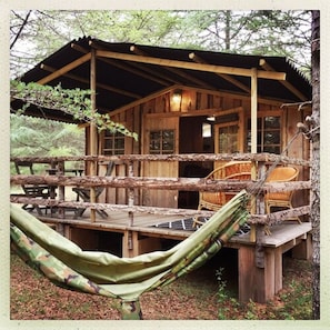 Une cabane en bois avec une véranda, un hamac et un coin repas.