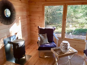 L’intérieur chaleureux d’un chalet avec un poêle à bois, un fauteuil confortable et une table agrémentée d’une lanterne décorative.