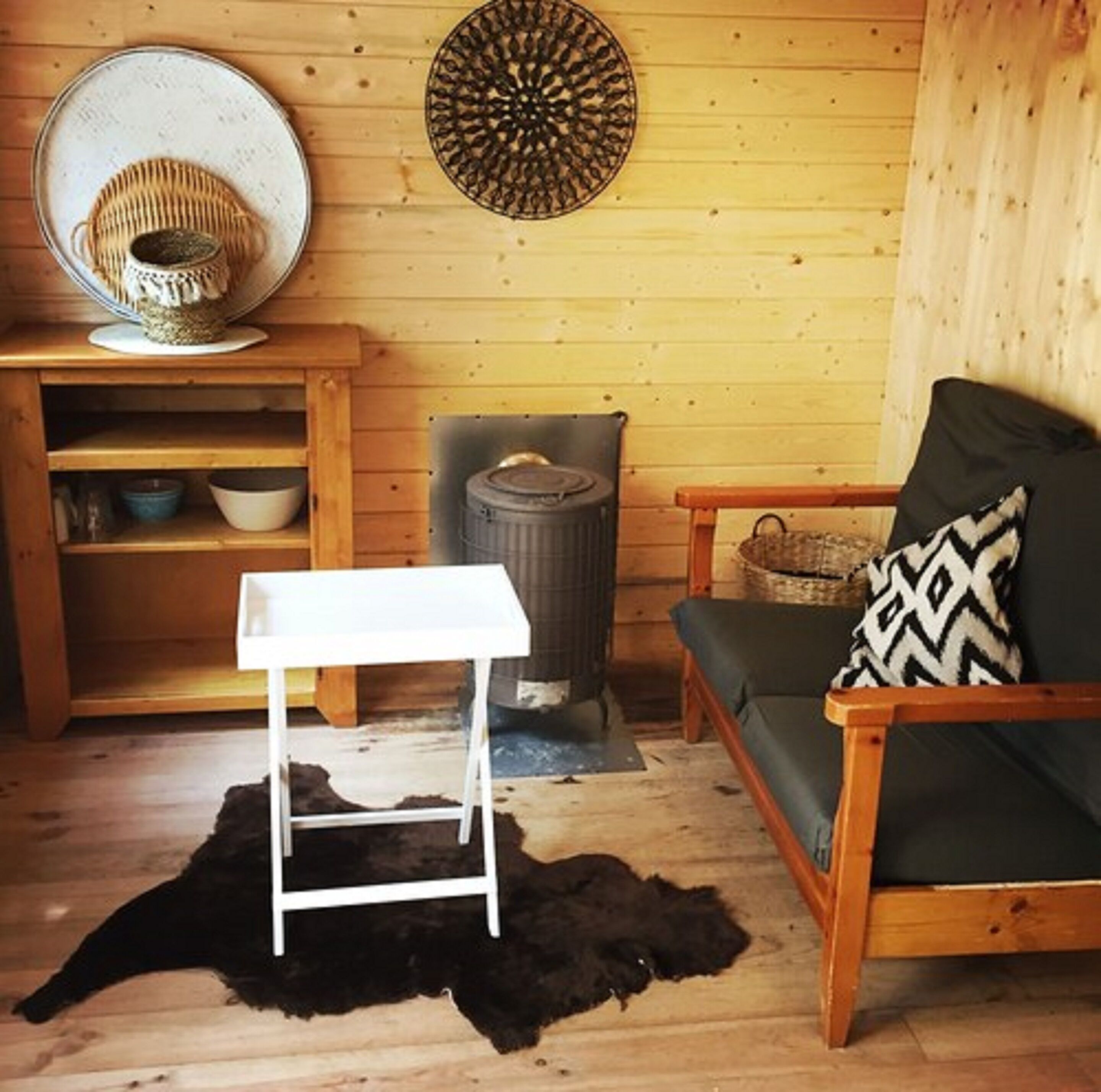 Une pièce chaleureuse avec un plancher en bois, une table blanche, un canapé agrémenté d’un coussin à motifs, une décoration murale et un petit radiateur.