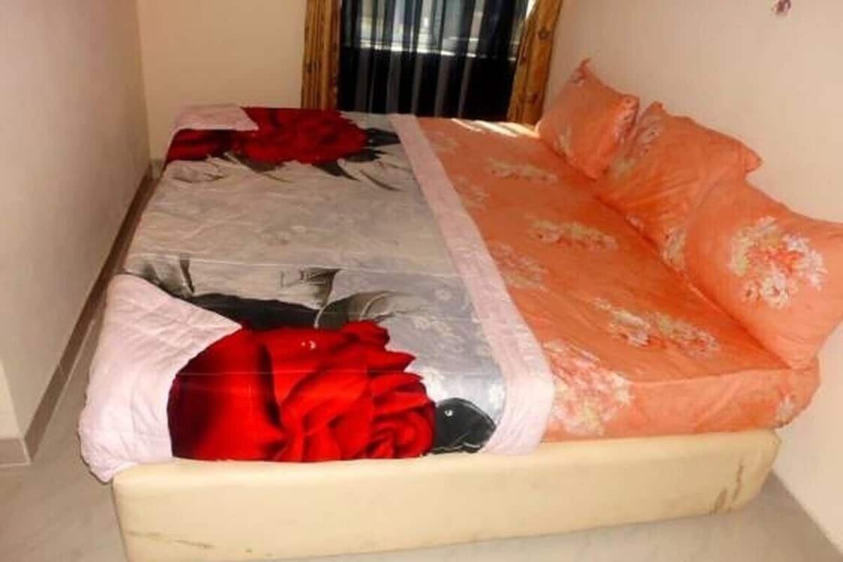 A bed with a floral bedspread, a red blanket, and an orange pillow.